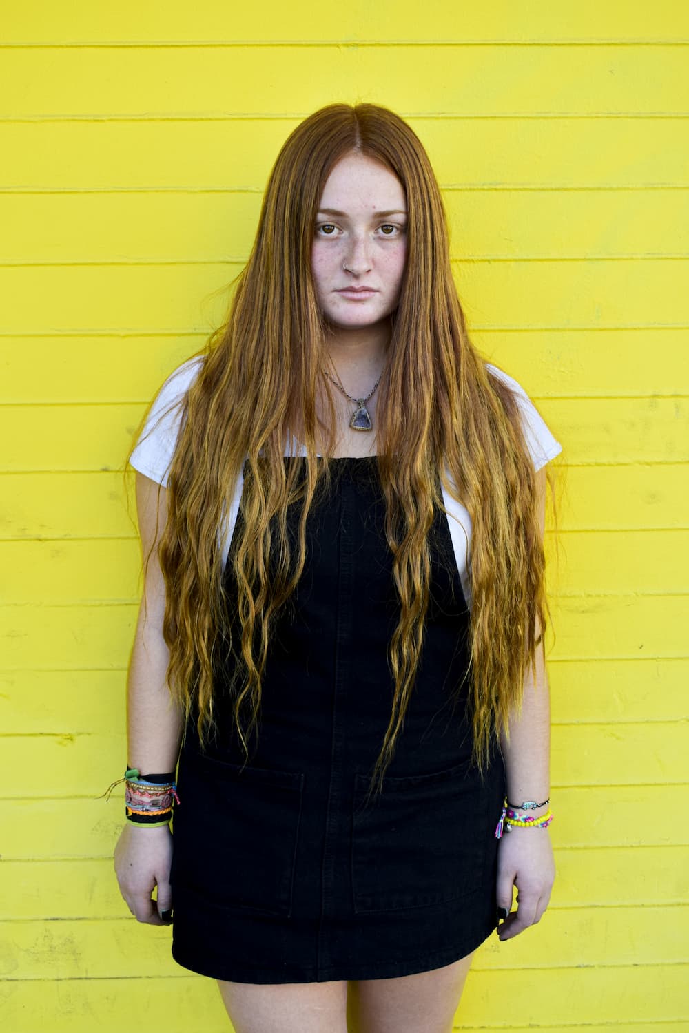 Fotografia de una joven peliroja parada frente a una pared amarilla